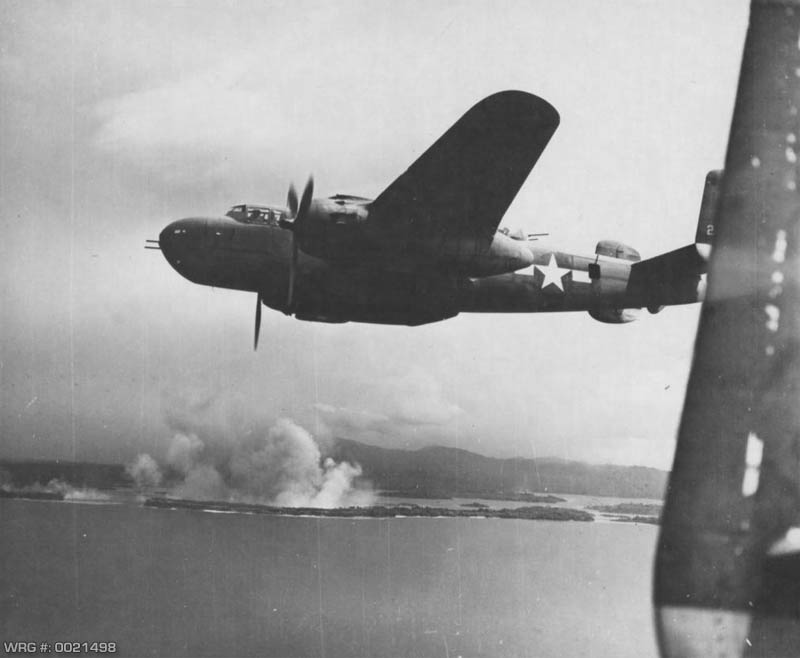 B-25 Mitchell over Cape Gloucester as bombs from other bombers burst on Japanese gun positions on New Britain, 1944. WRG #: 0021498